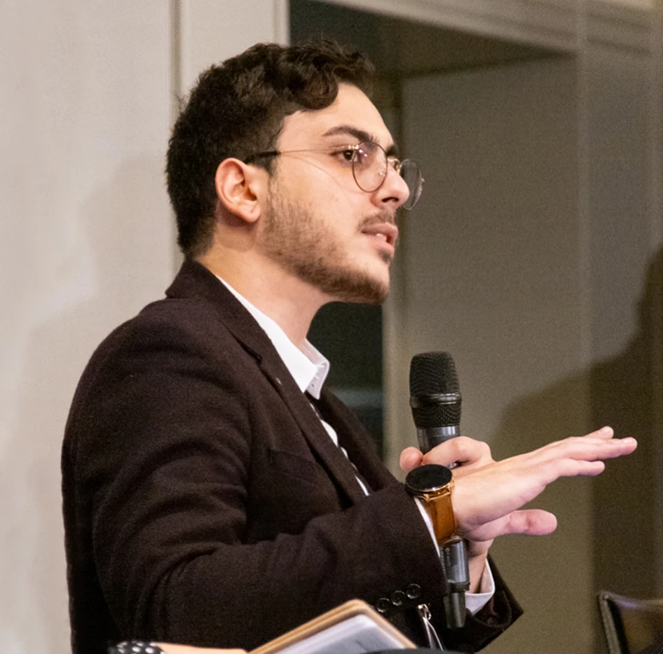 Jean Vella speaking into a microphone at an event.